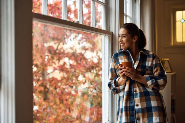 istock Happy woman looking through the window while drinking tea at home. 1440467964