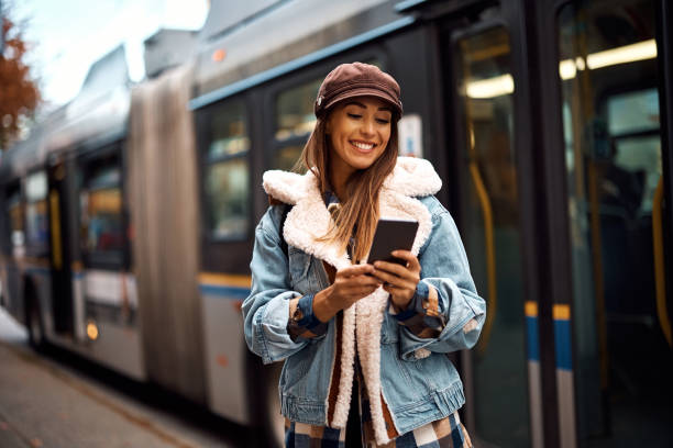 istock Happy woman using cell phone while getting out of public transport. 1440468542