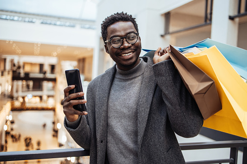 Handsome middle-aged black man with shopping bags enjoying in big shopping mall. Consumerism concept. Black Friday and holiday season.