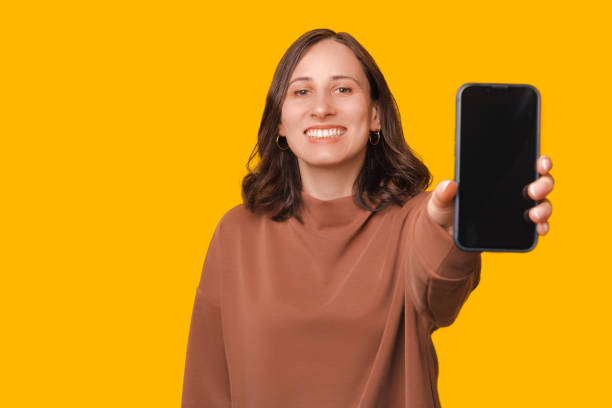 istock Joyful young student woman showing mobile phone over yellow background 1440468953