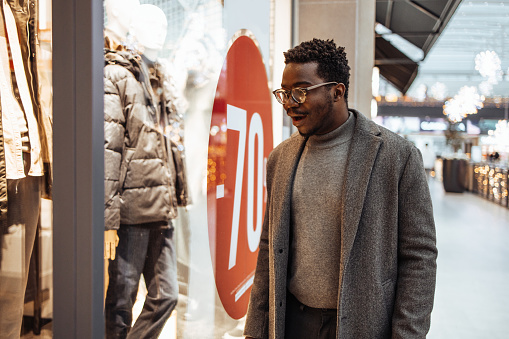 Handsome middle-aged black man with shopping bags enjoying in big shopping mall. Consumerism concept. Black Friday and holiday season.