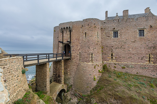 Bamburgh, England, United Kingdom – June 20, 2020: Bamburgh Castle is a medieval castle located on the coast of the North Sea along Bamburgh Beach in the village of Bamburgh. Today the castle is privately owned by the Armstrong family but is open to the public for sightseeing and events. This view is looking up from Bamburgh Beach.