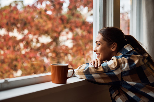 Young happy woman enjoying the view from her apartment window. Copy space.