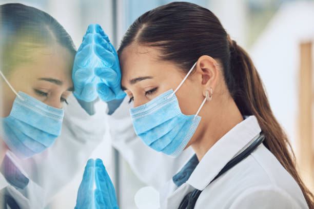 istock Young stressed and overworked doctor wearing mask and gloves while standing at a window in a hospital or clinic. One female only looking worried, hopeless and anxious while struggling with a challenge 1440471628