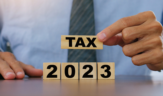 TAX in 2023 concept,Business man holding wooden block. State taxes,tax payment, governant ,finance, tax accounting, statistics and data analytic reserach,tax return, strategy plan, report.Business 2023 tax new year concept.