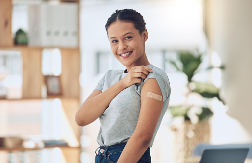 Young happy mixed race woman showing a bandaid on her arm after getting a covid vaccine. Portrait of a confident hispanic female smiling while showing a plaster on her arm after getting an injection