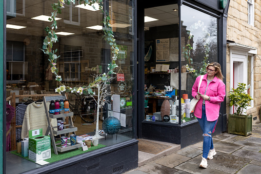 Full shot of a female walking past an eco shop front on her phone looking in through the shop windows. She is wearing a vibrant pink jacket.