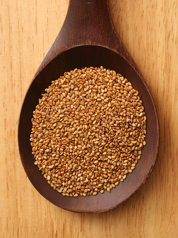 Top view of wooden spoon with golden sesame seeds on it