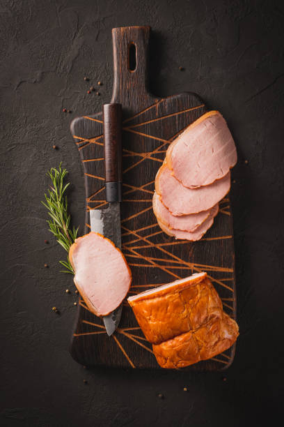 istock Spicy smoked ham with rosemary and kitchen knife on a black stone table 1440475918