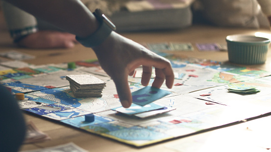 Family fun afternoon. Playing a board game with cards and dice. Hand moving the pieces on the game board.