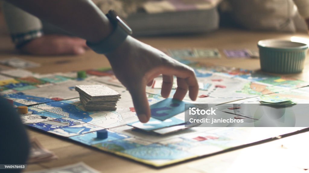 African ethnicity human hand picking up game card on a game board. Diverse family game night Family fun afternoon. Playing a board game with cards and dice. Hand moving the pieces on the game board. Board Game Stock Photo