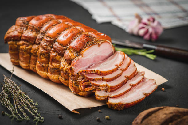 istock Spicy smoked ham with rosemary and kitchen knife on a black stone table. Pork roll 1440476464