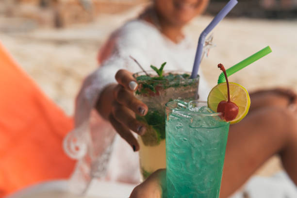 istock Hands of unrecognizable people making a toast with a mojito and an alcoholic cocktail type drink while sitting on the beach. 1440479732