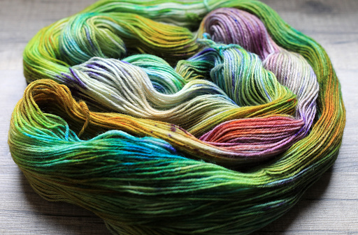 Beautiful skein of colourful handdyed sockyarn for knitting, laying on a wooden floor as a background