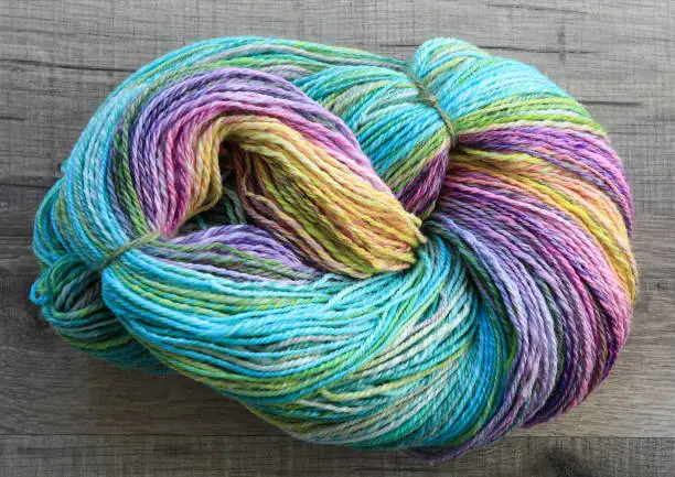 Beautiful skein of colourful handdyed handspun yarn for knitting, laying on a wooden floor as a background