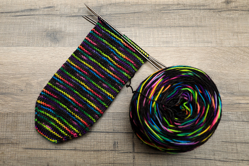 knitting a colourful black and rainbow sock lyaing on a wood floor