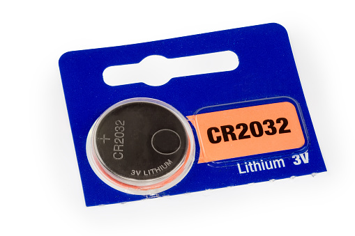 Lithium button battery CR2032 type with voltage and polarity designation in the commercial packaging on a white background close-up