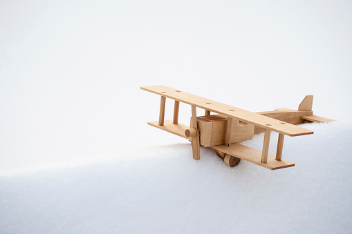 A wooden toy model of an airplane in the snow, against the background of a winter forest. The concept of travel, tourism. Beautiful winter background or postcard. Dream of a journey.