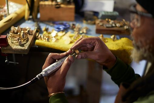Jeweler, black man and metal worker working on jewelry for a hobby or profession in a garage. Construction tool, handy work and employee craft to make a ring from gold in a warehouse or factory