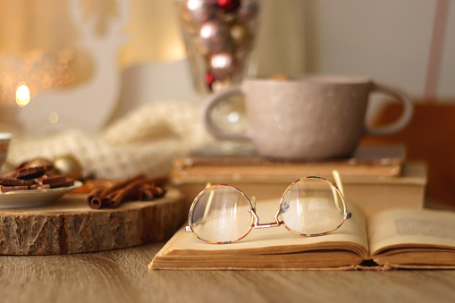 Cup of tea or coffee, various sweets and spices, Christmas decorations, comfy blanket, books and glasses. Selective focus.