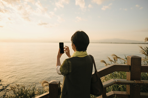 Asian mature adult woman photographing the sunset in Enoshima Island, Japan