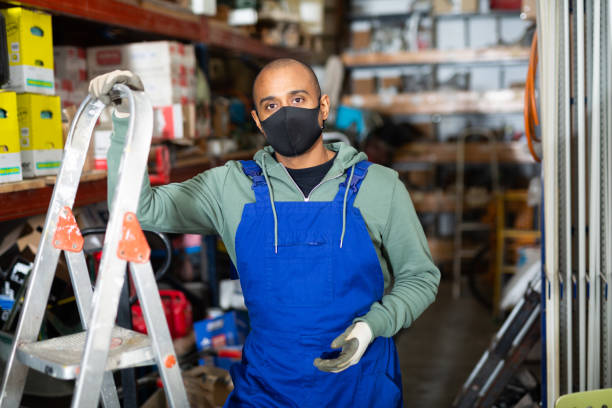 istock Warehouse worker in protective mask stands next to stepladder and tool shelves in hardware store 1440486064