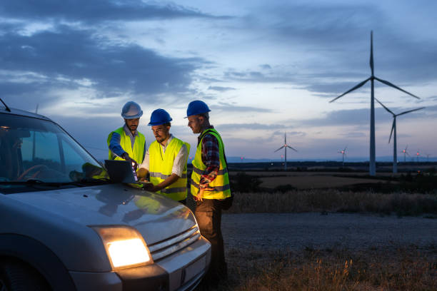 istock Group of engineers and maintenance workers using laptop together discussing plans in wind turbine farm at sunset. 1440486172