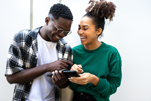 Young african american couple laughing together using smart phones. Having fun.Technology concept.