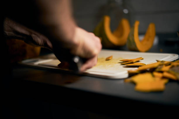 istock Man cuts a cool round pumpkin into small pieces with a dark background. 1440486263