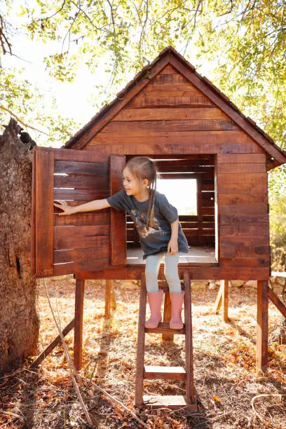 Photo of Girl plays in creative handmade treehouse in backyard, summer activity, happy childhood, cottagecore