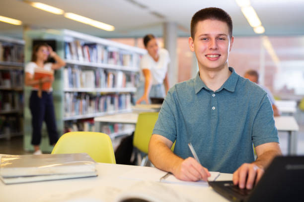 istock Concentrated young man spending time in library, reading books and making laptop 1440488212