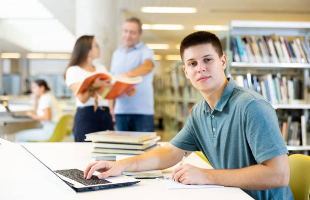 istock Focused casual young male writing in planner and using laptop in the library 1440488268