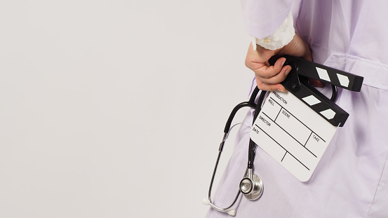 Clapper board and stethoscope in doctor's hand on white background. Studio shooting.