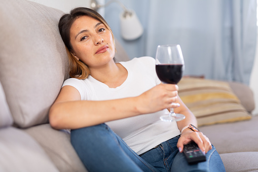 Colombian woman is resting with wine and watching TV at home
