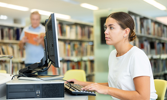 Adult female student in to public library is looking for information about books in a computer