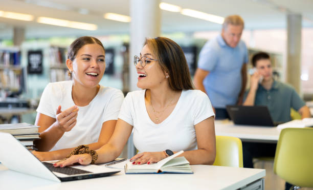 istock Two friendly adult female students studying in university library, using books and laptop while preparing for lecture 1440490048