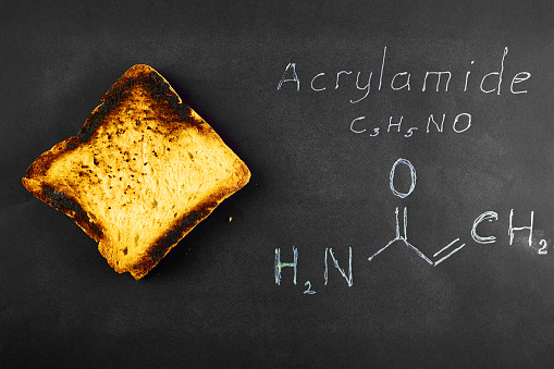 inscription chemical formula of acrylamide and black burnt bread toast containing acrylamide on a black background