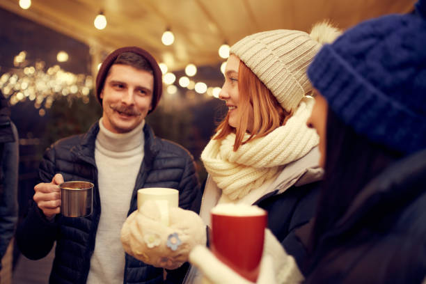 istock Group of young people spending time together, drinking mulled wine, talking, laughing at winter fair at evening time. Winter holidays, Christmas vibes concept 1440491245