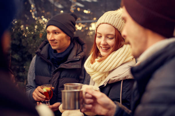 Fun, joy, party. Group of young people spending time together, drinking mulled wine, talking, laughing at winter fair at evening time. Youth dressing warmly. Winter holidays, Christmas vibes concept