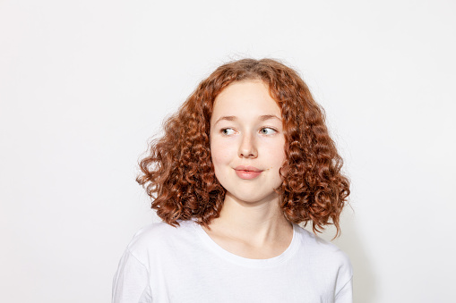 Close-up studio portrait of a cheerful red-haired teenage girl in a white t-shirt on a white background