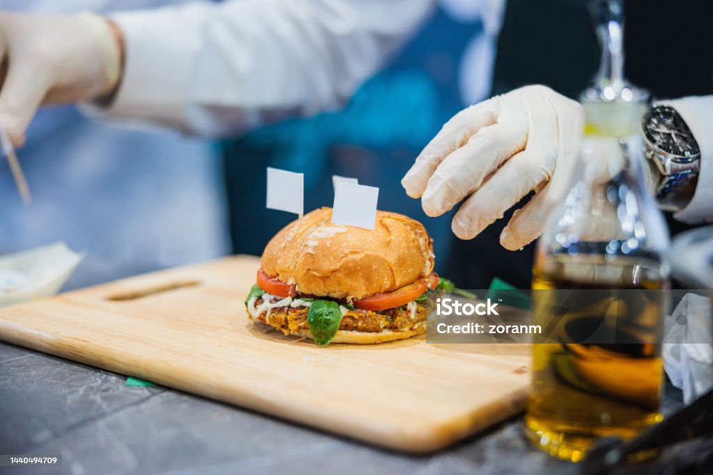 Serving prepared and labeled veggie burger on wooden board Wearing protective gloves and serving labeled veggie burger on wooden board Bun - Bread Stock Photo