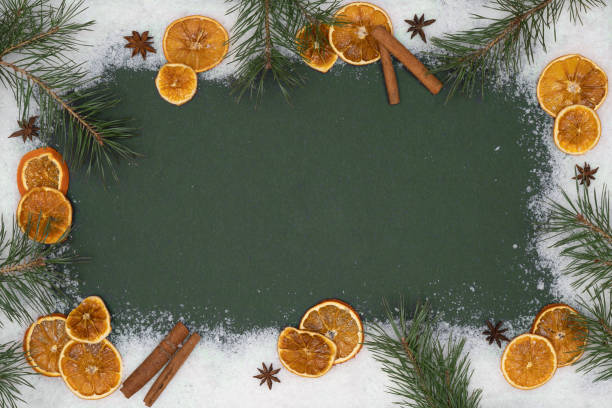 istock Festive christmas advent celebration holidays background banner greeting card - Border frame made of christmas ornaments, dried orange slices, cinnamon sticks, star anise, pine branches and snow on sk green table texture,  top view 1440497230