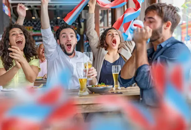 Photo of Group of soccer fans friends celebrating goal in pub with national flag