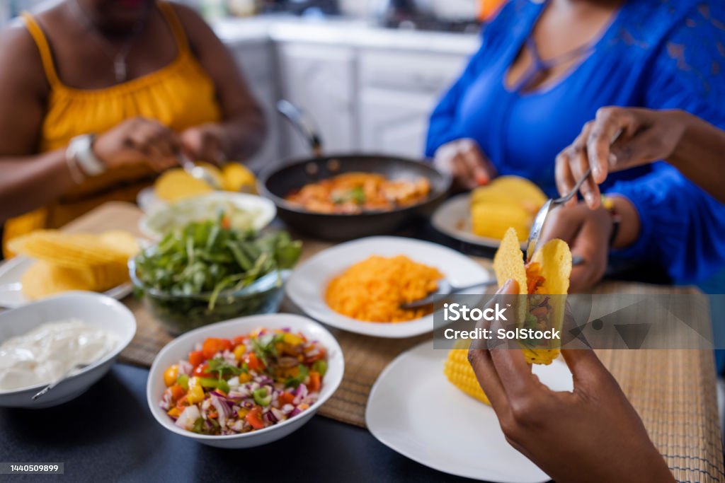 Excited for Their Tacos An unrecognisable family sitting at a dining table together, ready to start eating tacos at home in Newcastle upon Tyne, England. The main focus is one woman filling her taco shell with peppers and onions. Taco Stock Photo