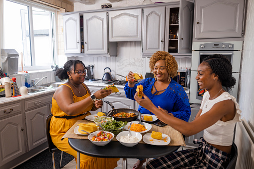 A woman and her two daughters sitting at a dining table together, ready to start eating dinner at home in Newcastle upon Tyne, England. They are all holding their tacos in the air and smiling, exited to eat them.