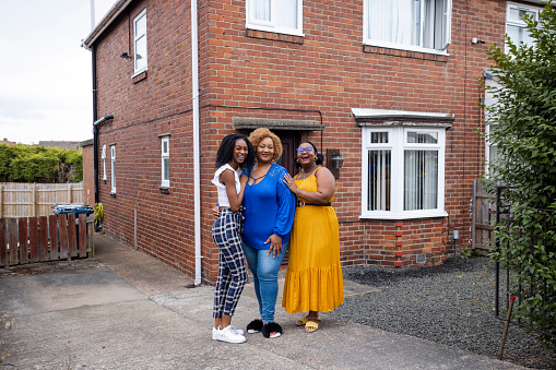 A portrait of a family standing outside their home in Newcastle upon Tyne, England. They looking at the camera and smiling while standing side by side.