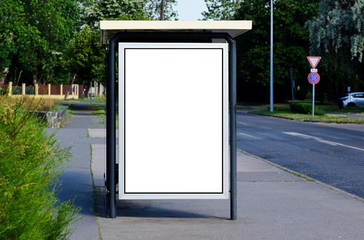 image composite of bus shelter at a bus stop. empty milky white poster ad and advertising display glass and light box. clear safety glass design.  aluminum frame structure. street perspective with trees. green background with trees.