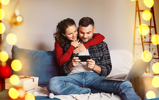 Happy young married couple together using their smart phone while at home and enjoying christmas holiday.
