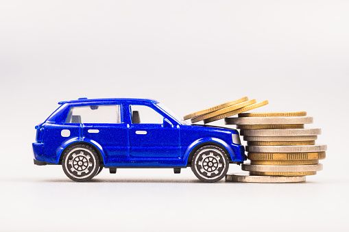 A small blue car hit the stack of money coins at the front, car accident and insurance, compensation, car finance problem, car maintenance, or penalty offense