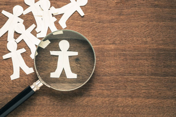 istock Magnifying glass on paper human dolls, only one is in focus 1440513712